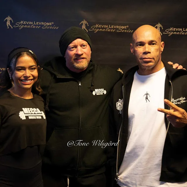 Tre personer poserer foran en vegg med «Kevin Levrone Signature Series»-logo under et treningsarrangement.
