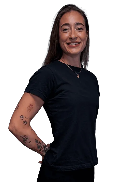 En smilende kvinne i svart t-skjorte står med hånden på hoften og viser tatoveringer på armen.